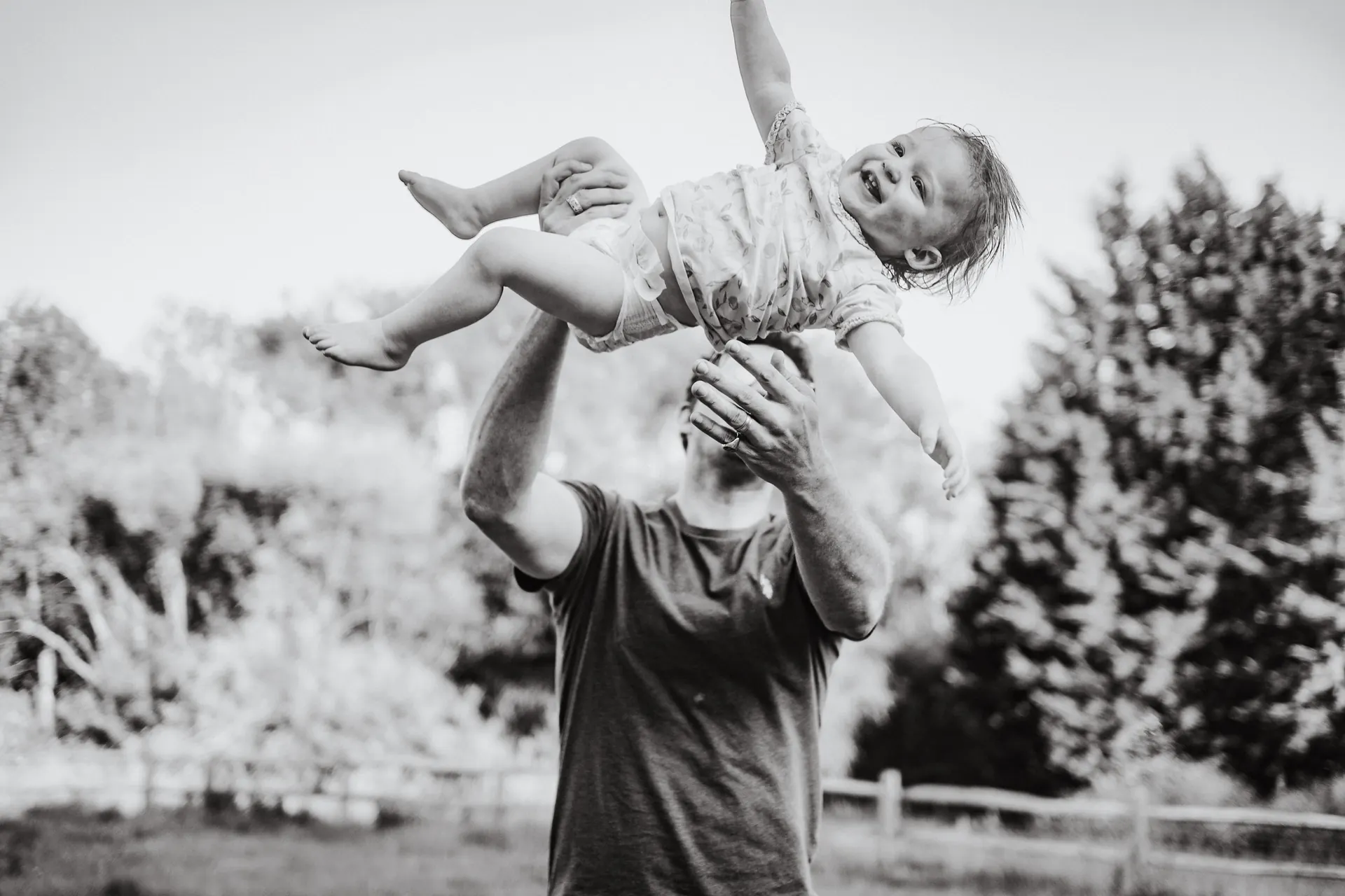 Father lifting his laughing baby into the air outdoors