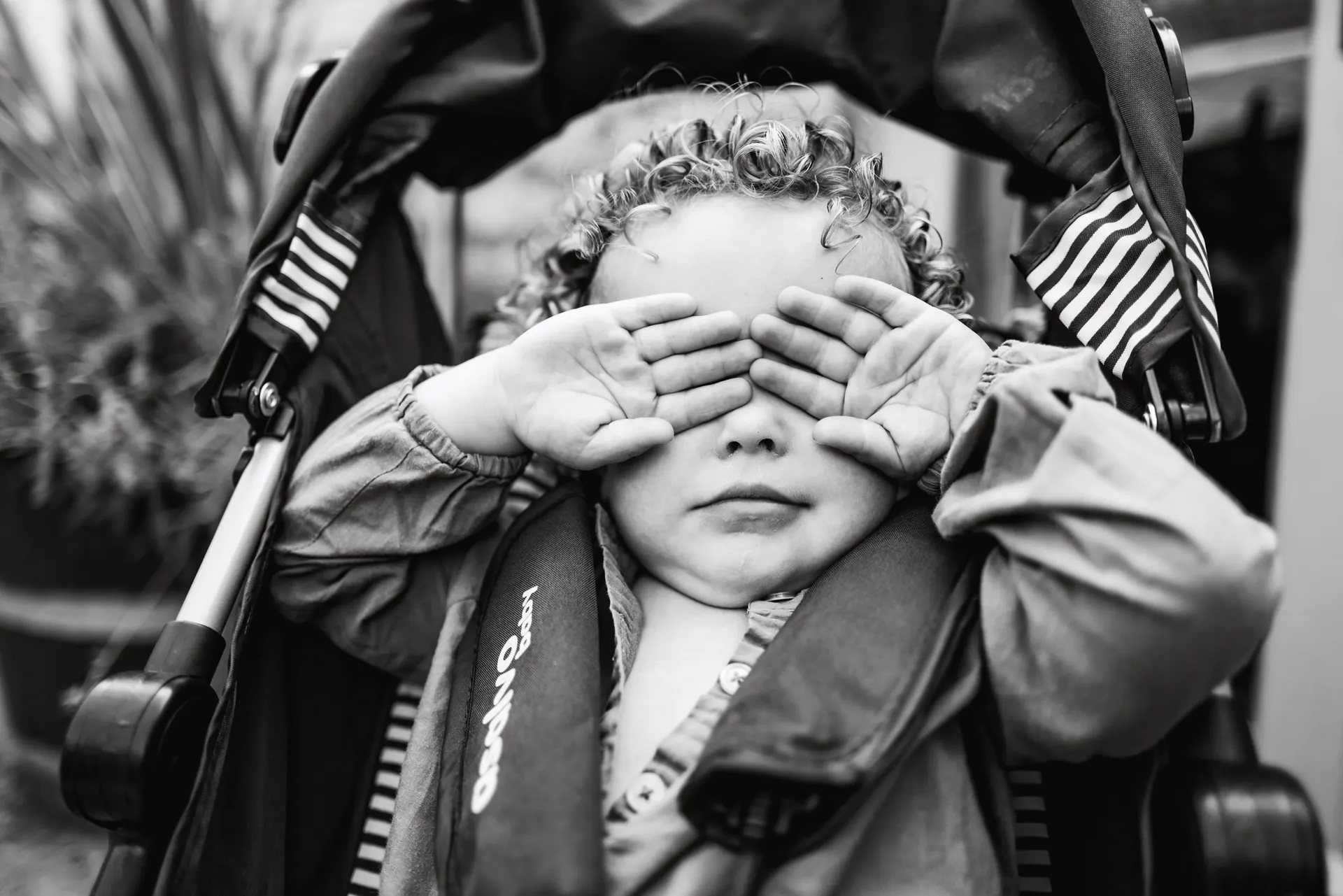 Toddler in a pushchair playing peek-a-boo with hands over their eyes