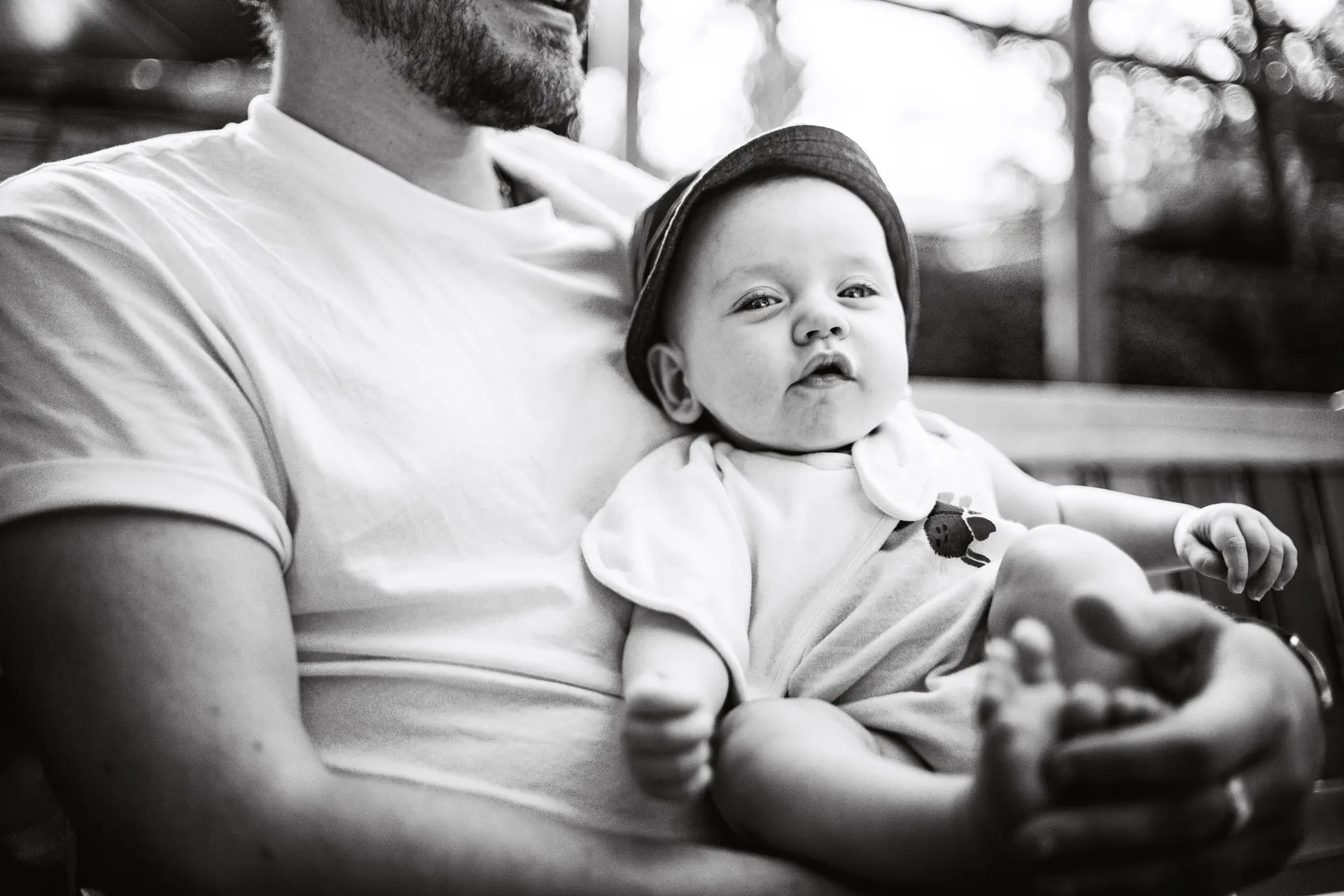 Baby in a sun hat relaxing on their father's lap