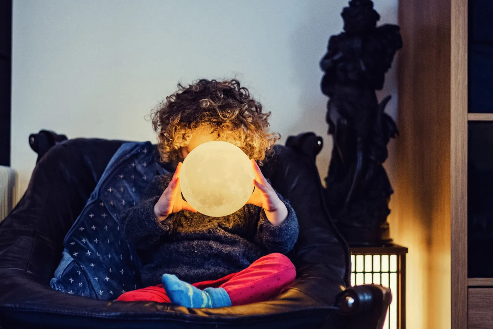 Child holding a glowing moon lamp at home
