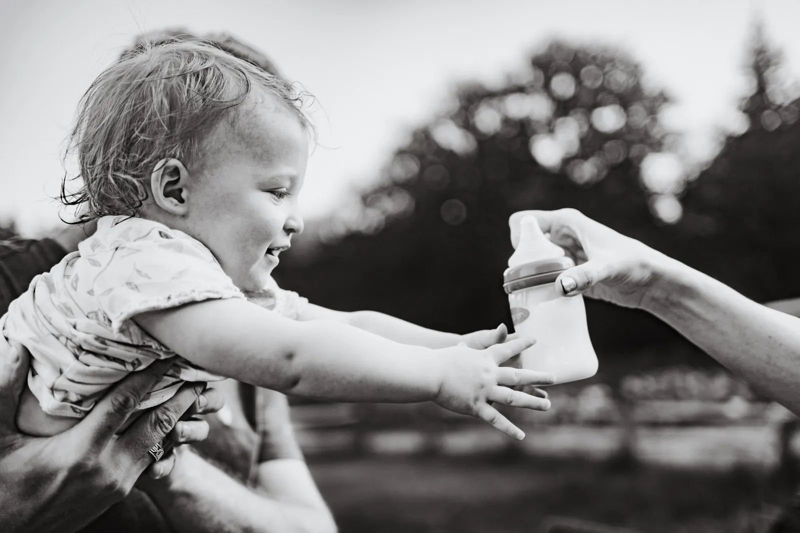 Baby reaching for a bottle outdoors, black and white