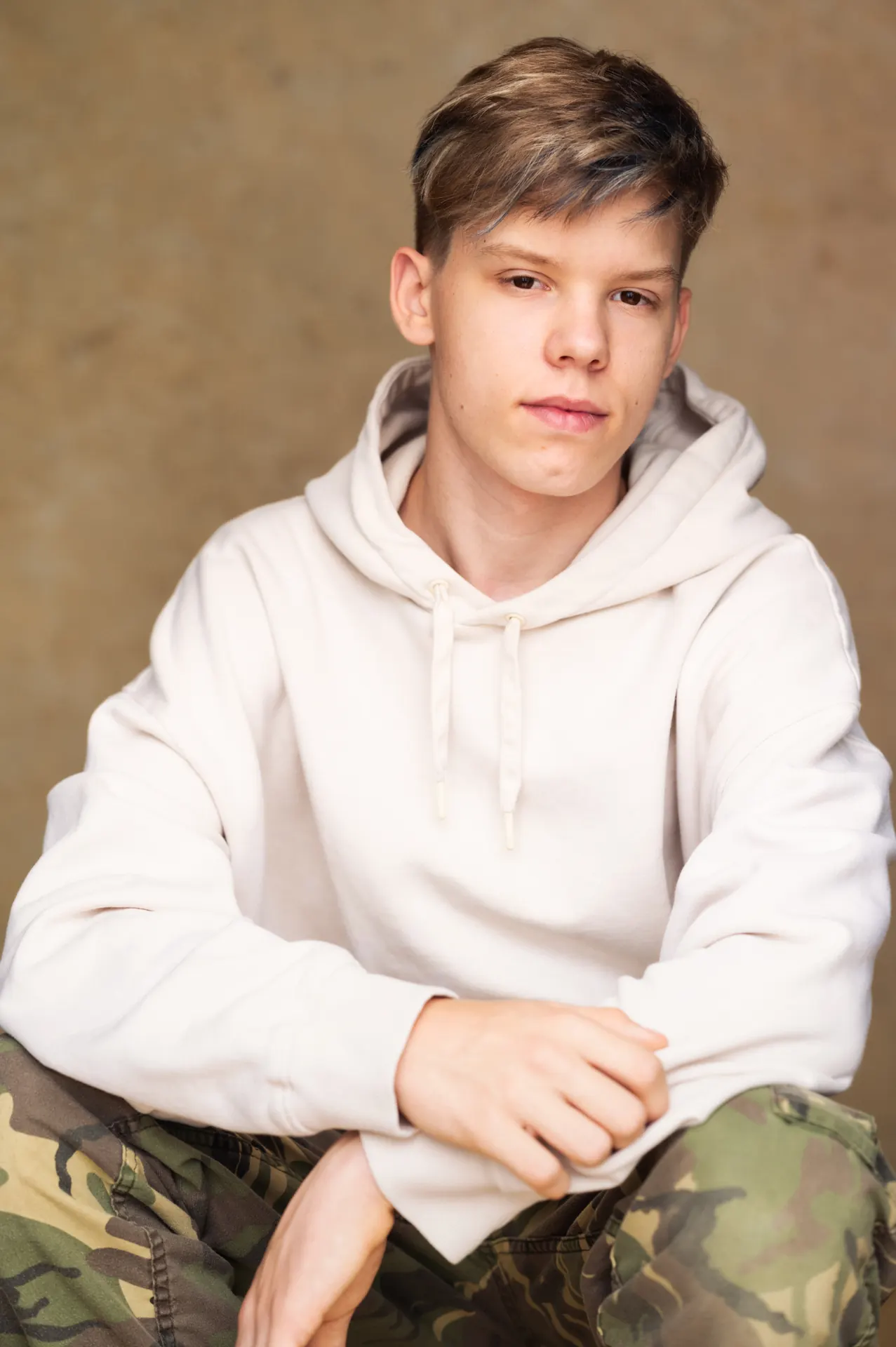 Teenage boy in a cream hoodie sitting for a portrait