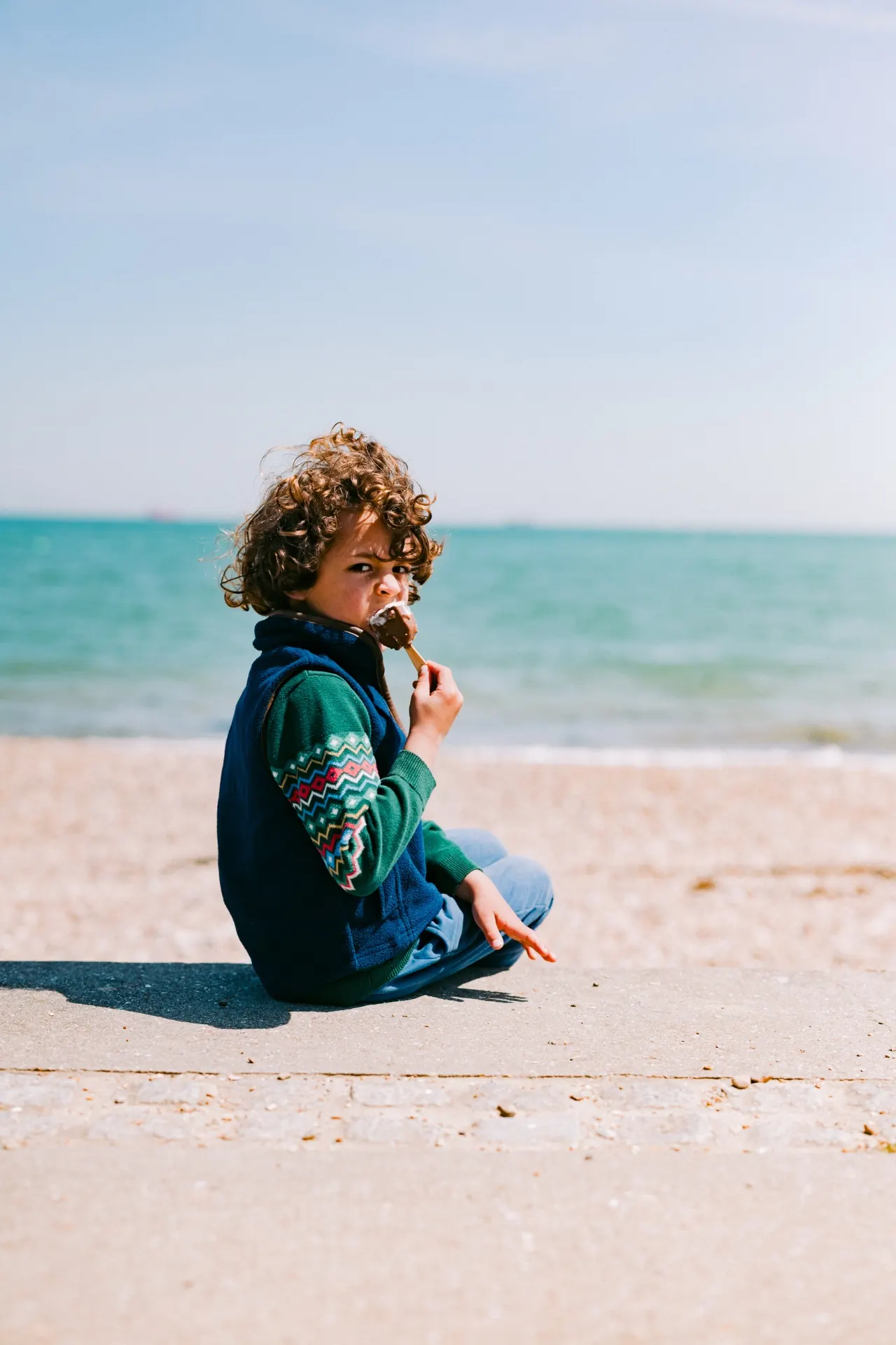 Curly-haired boy eating ice cream by the sea