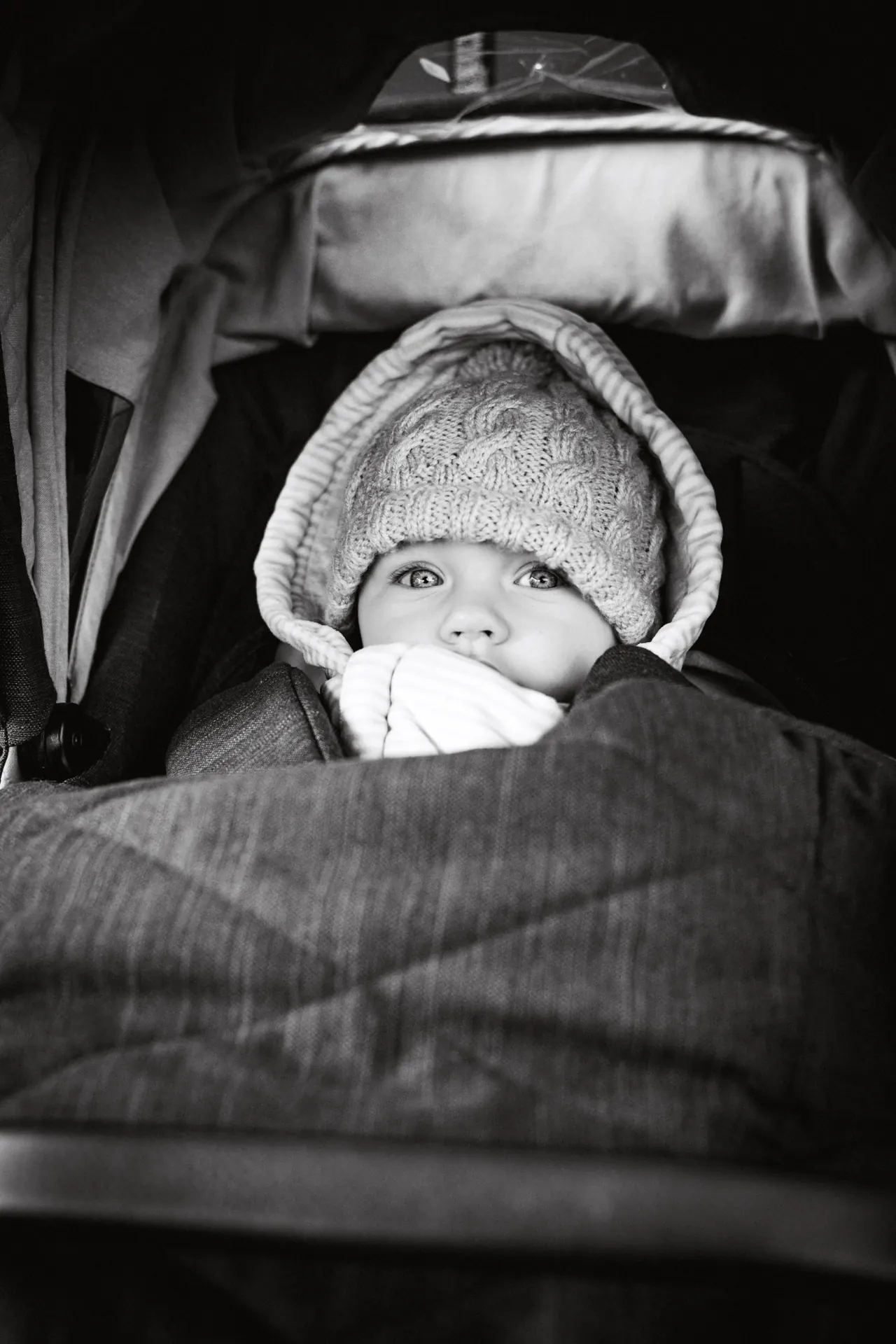 Baby in knitted hat peeking from pram, black and white