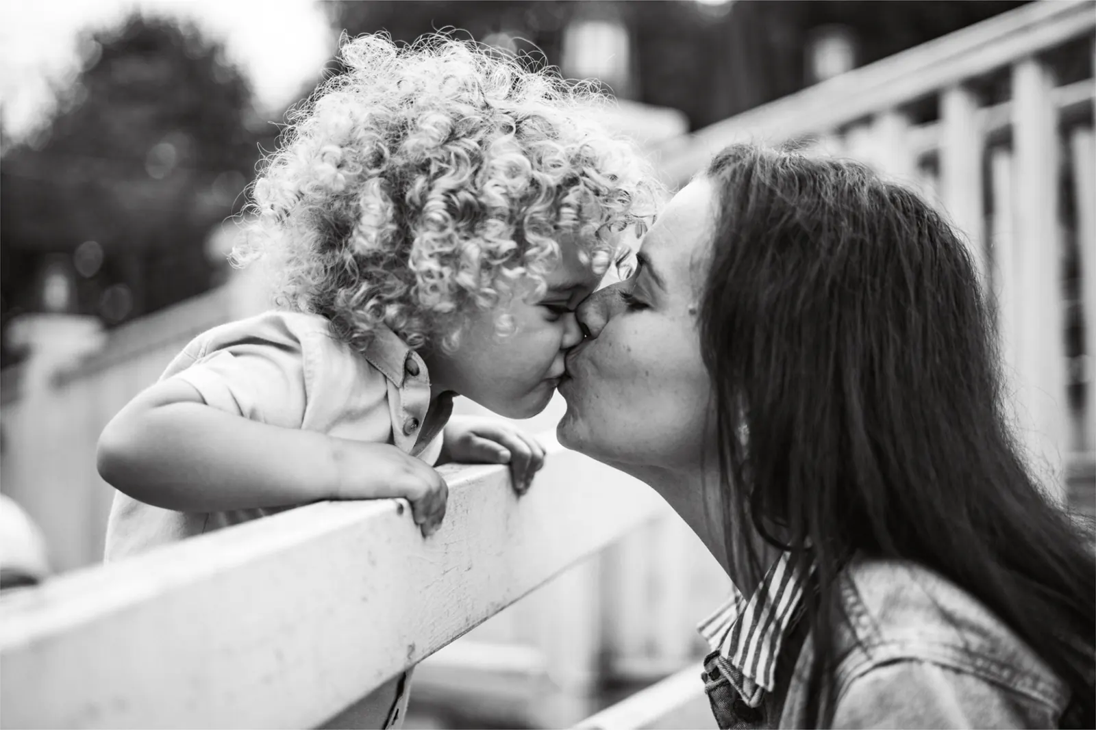 Mother kissing curly-haired toddler, black and white