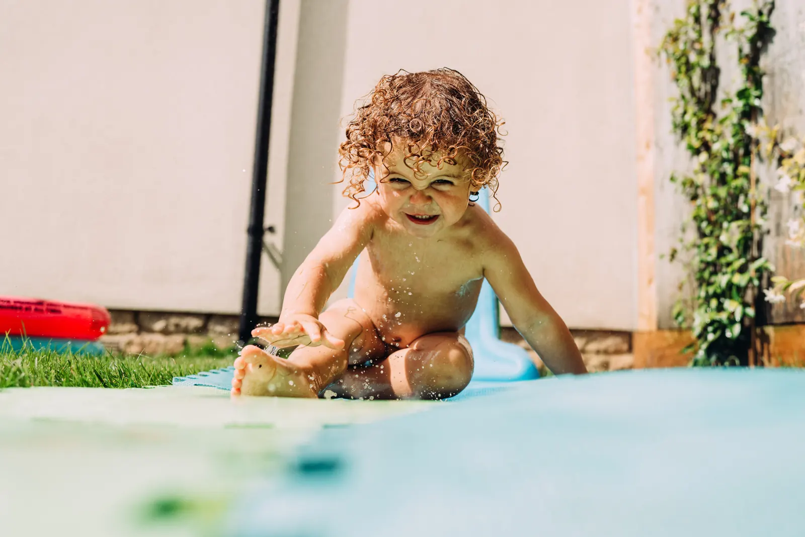 Curly-haired child splashing on a garden water slide