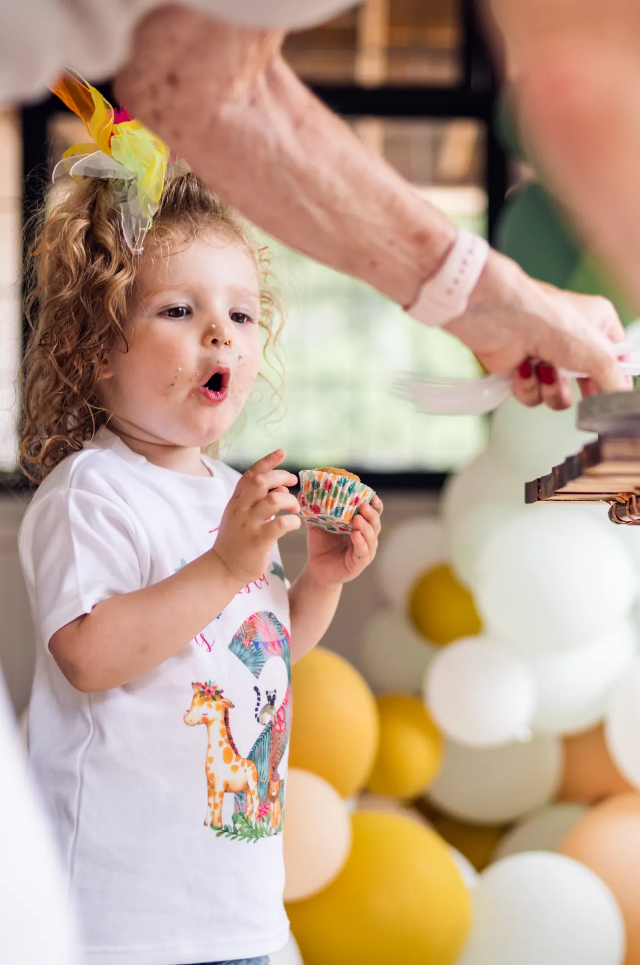 Curly-haired toddler eating a cupcake at a birthday party