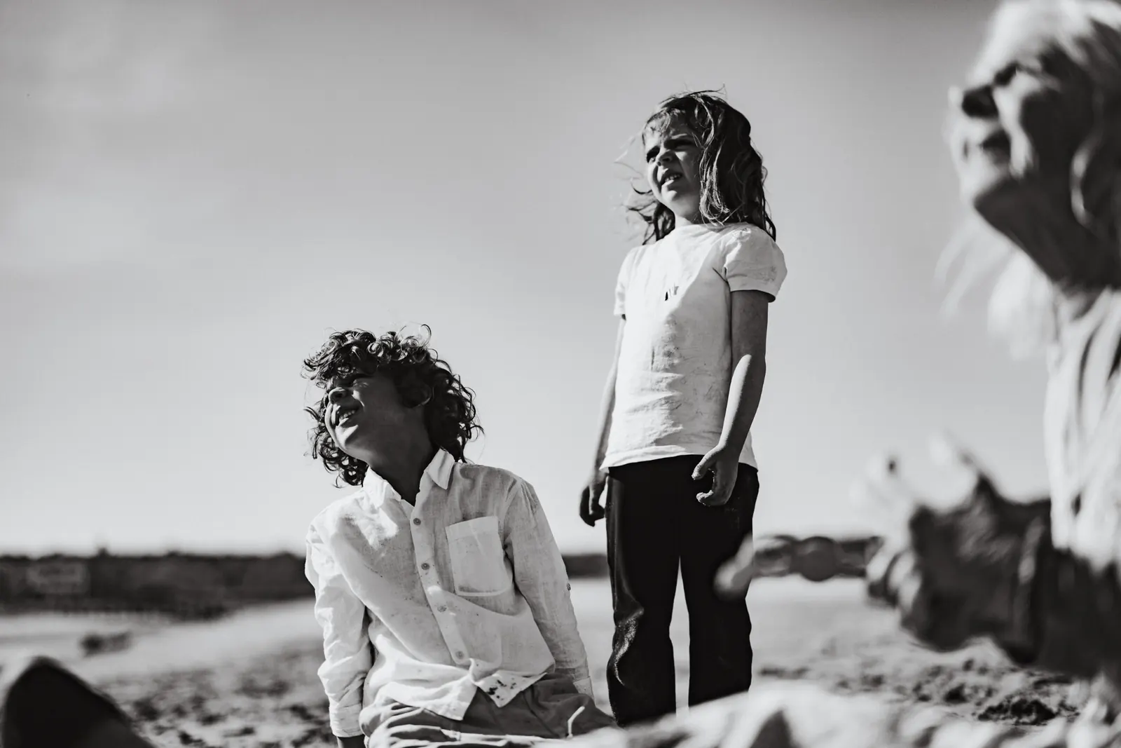 Two children laughing on a windy beach, black and white