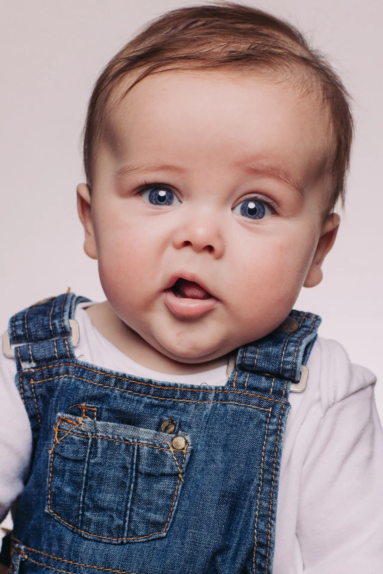 Baby with bright blue eyes in denim overalls
