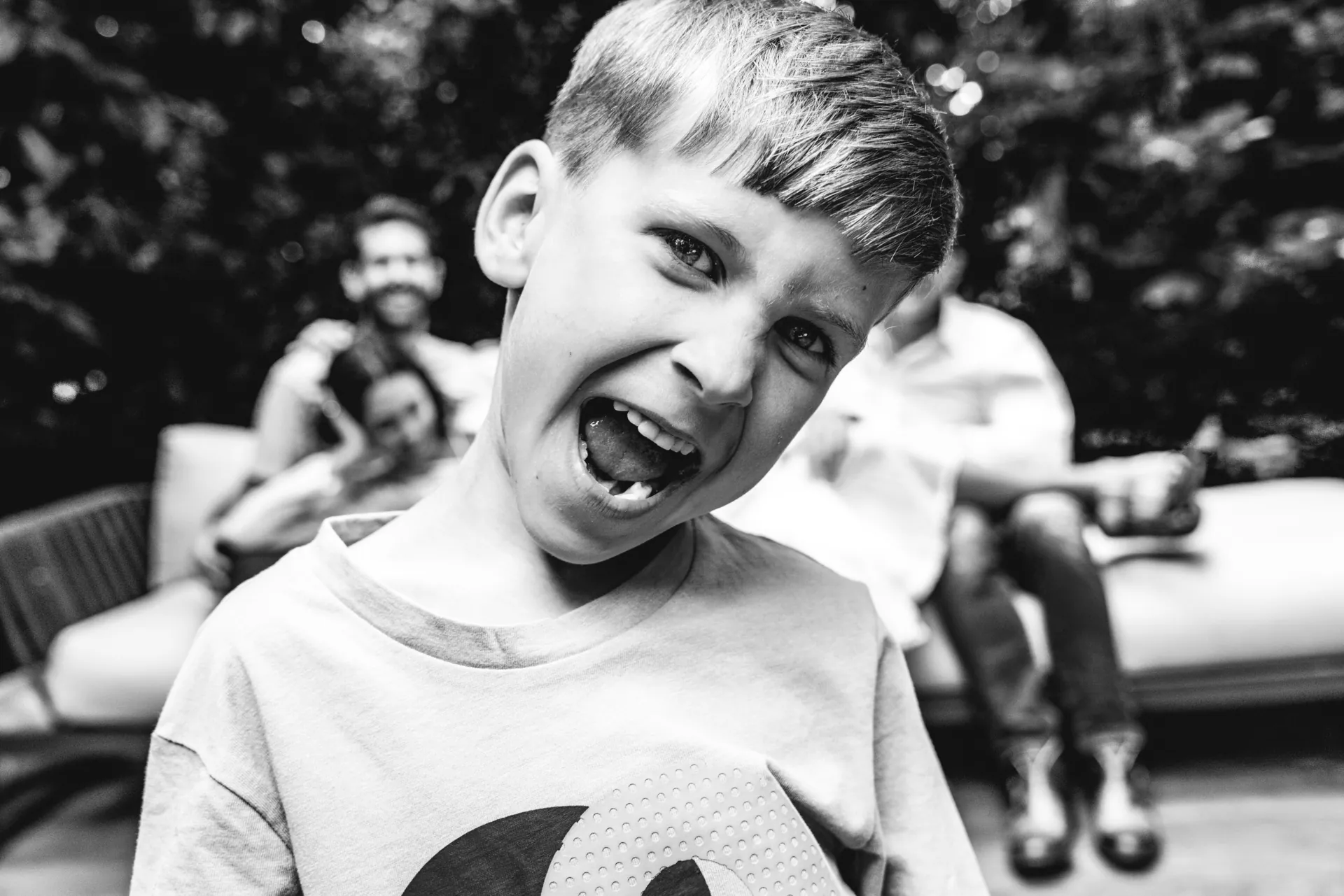 Black and white portrait of a laughing boy with his family in the background