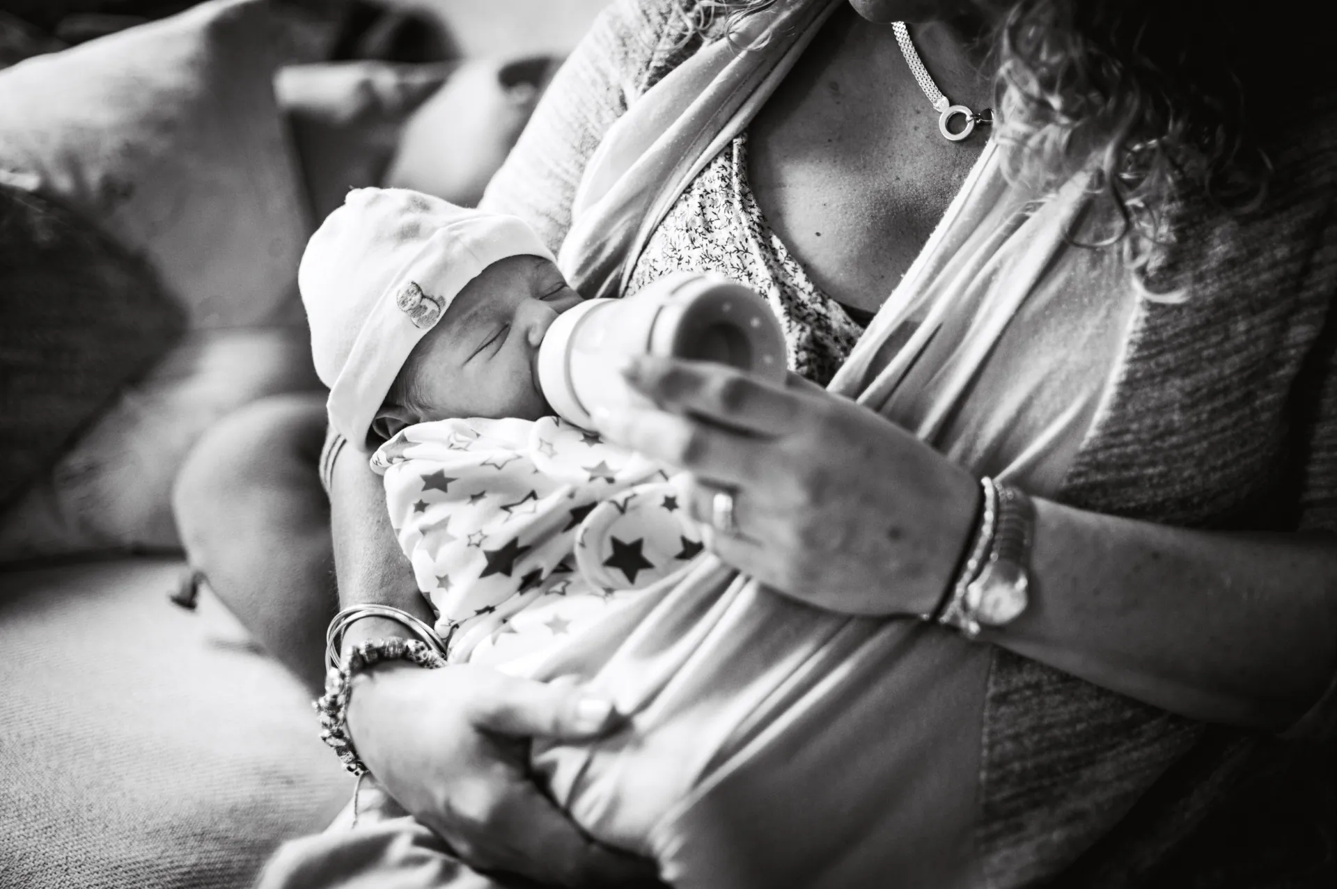 Black and white photo of a newborn in a star-print outfit being bottle-fed at home