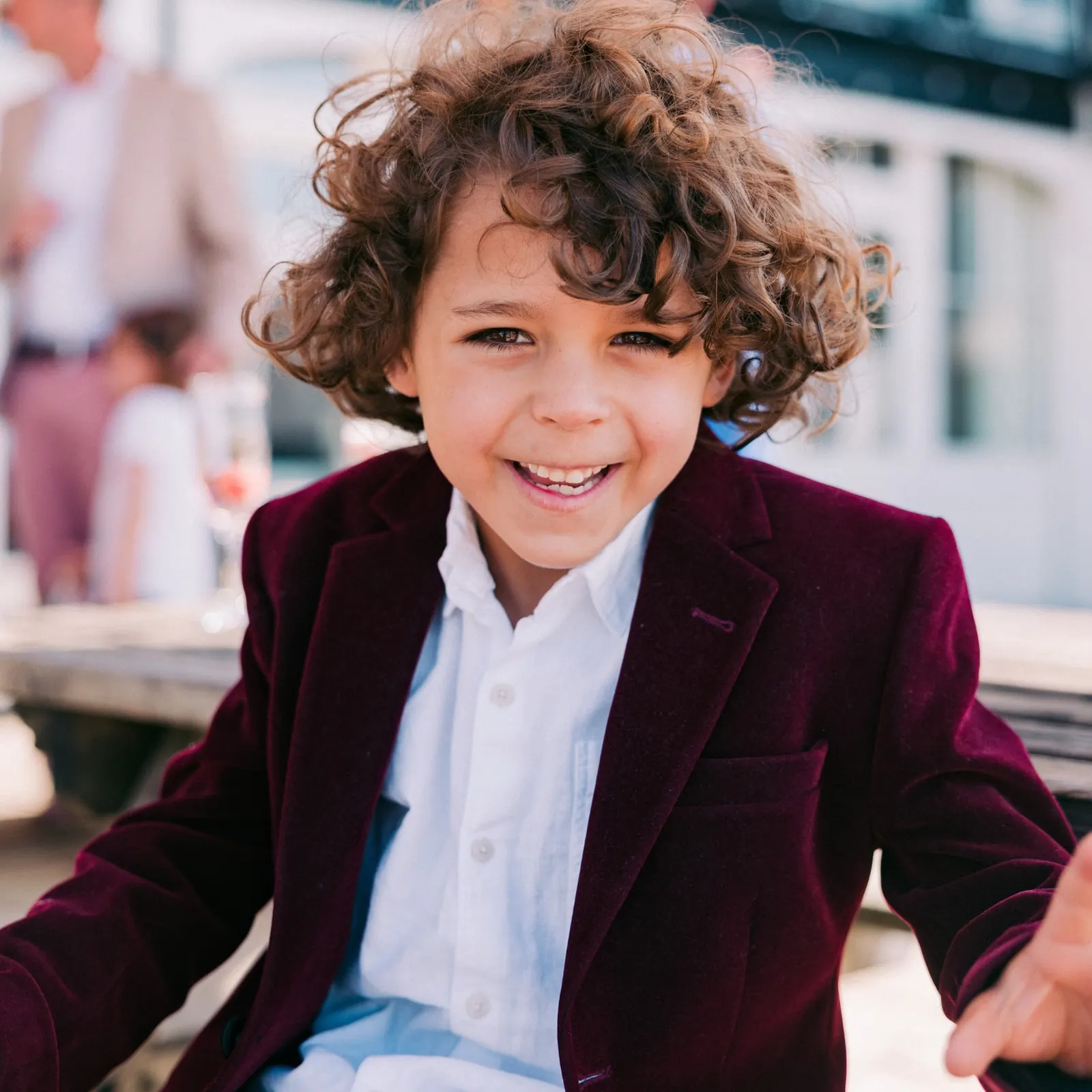 Smiling young boy with curly hair in a burgundy velvet blazer