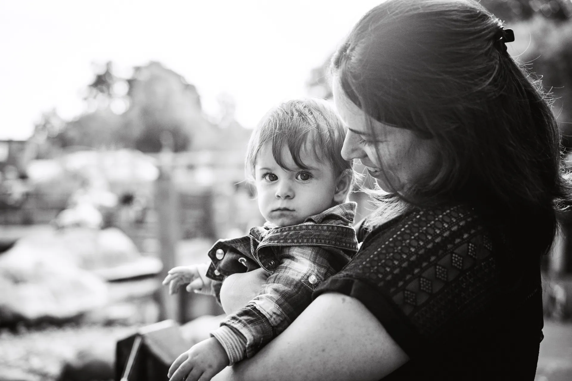Black and white photo of a mother holding her toddler outdoors in bright light
