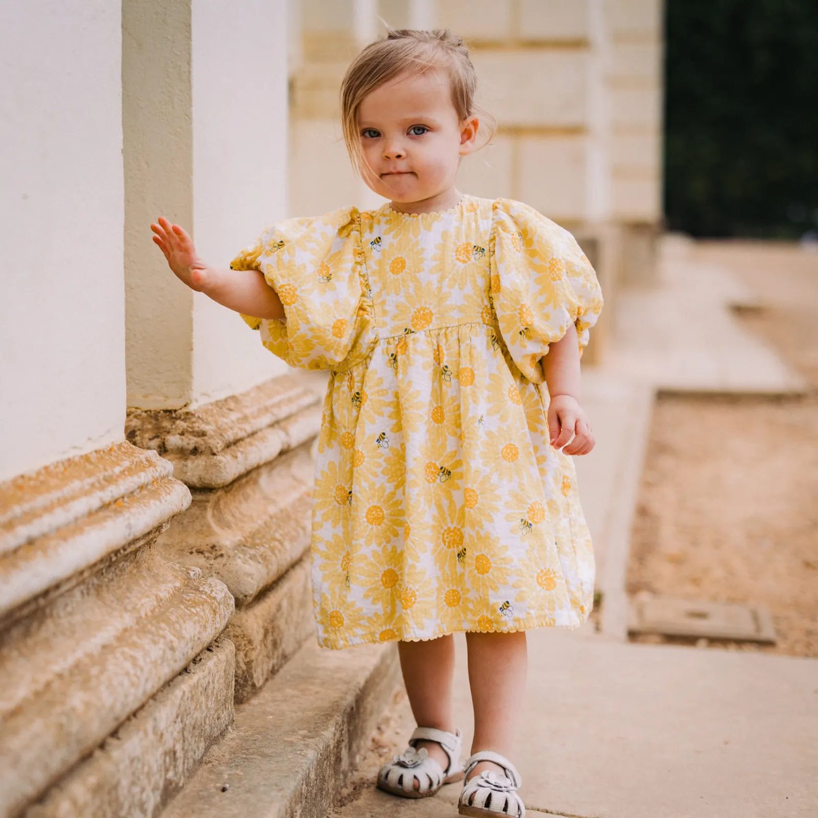 Toddler in a yellow floral dress standing on stone steps outdoors