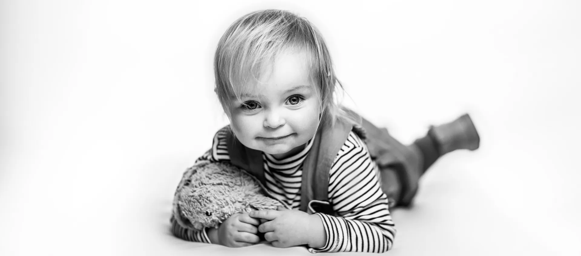 Black and white studio portrait of a toddler lying on the floor with a soft toy