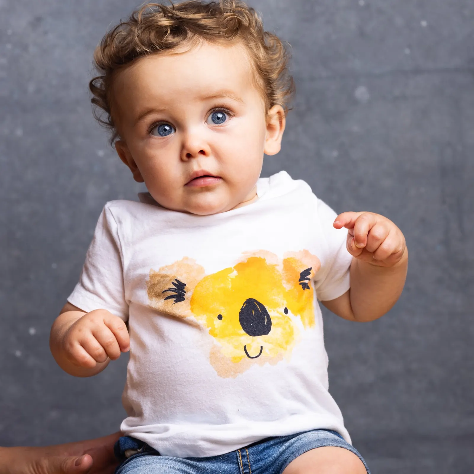 Curly-haired toddler in a white koala t-shirt looking up curiously